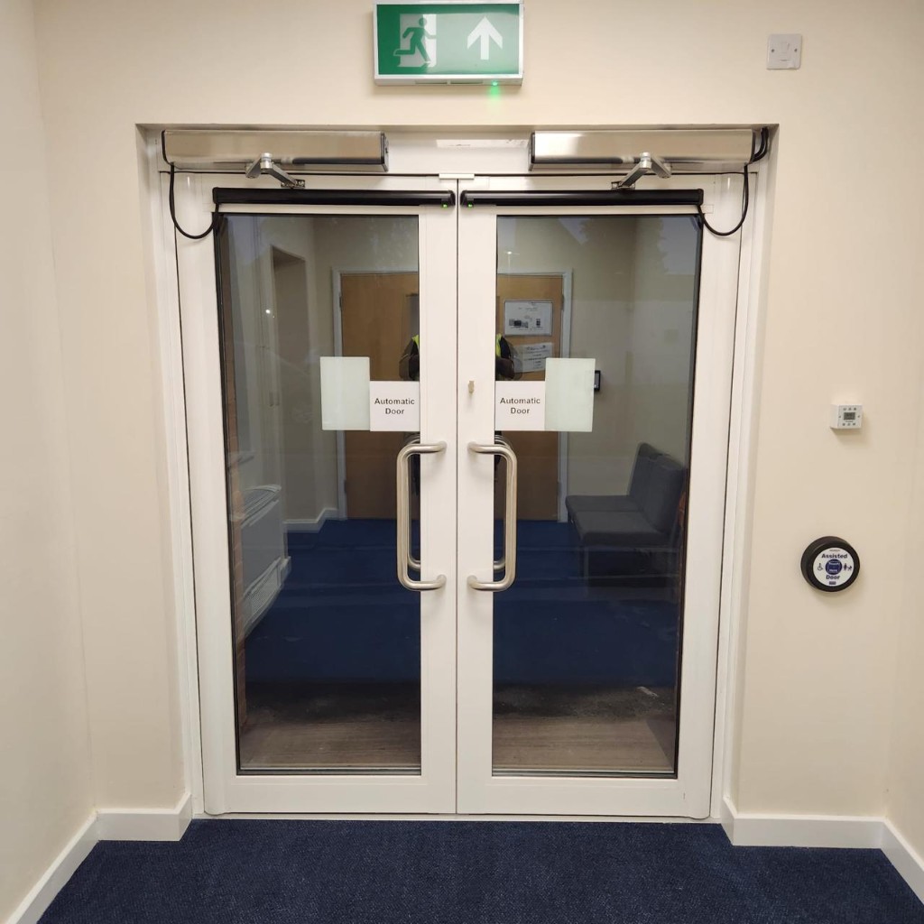 White-framed automatic swing doors with overhead operators, accessibility push pad and emergency exit signage