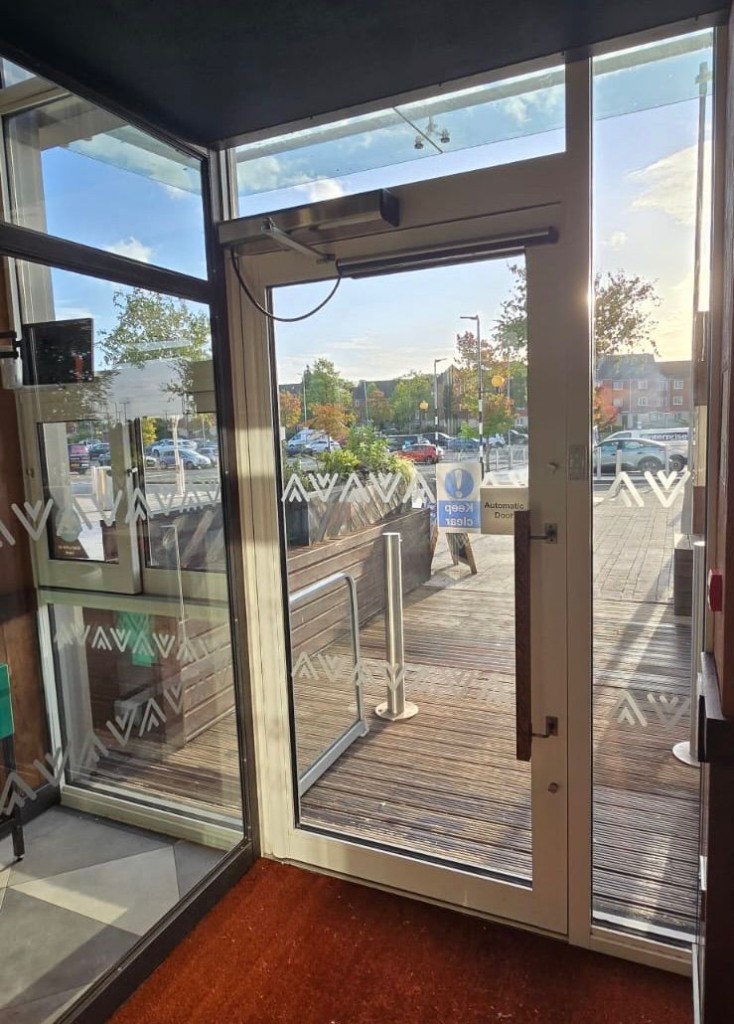 Automatic swing door operator unit & arm on a white-framed commercial entrance