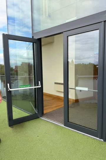 Anthracite aluminium double fire exit doors with panic bars and push bar to open signage at a commercial building entrance