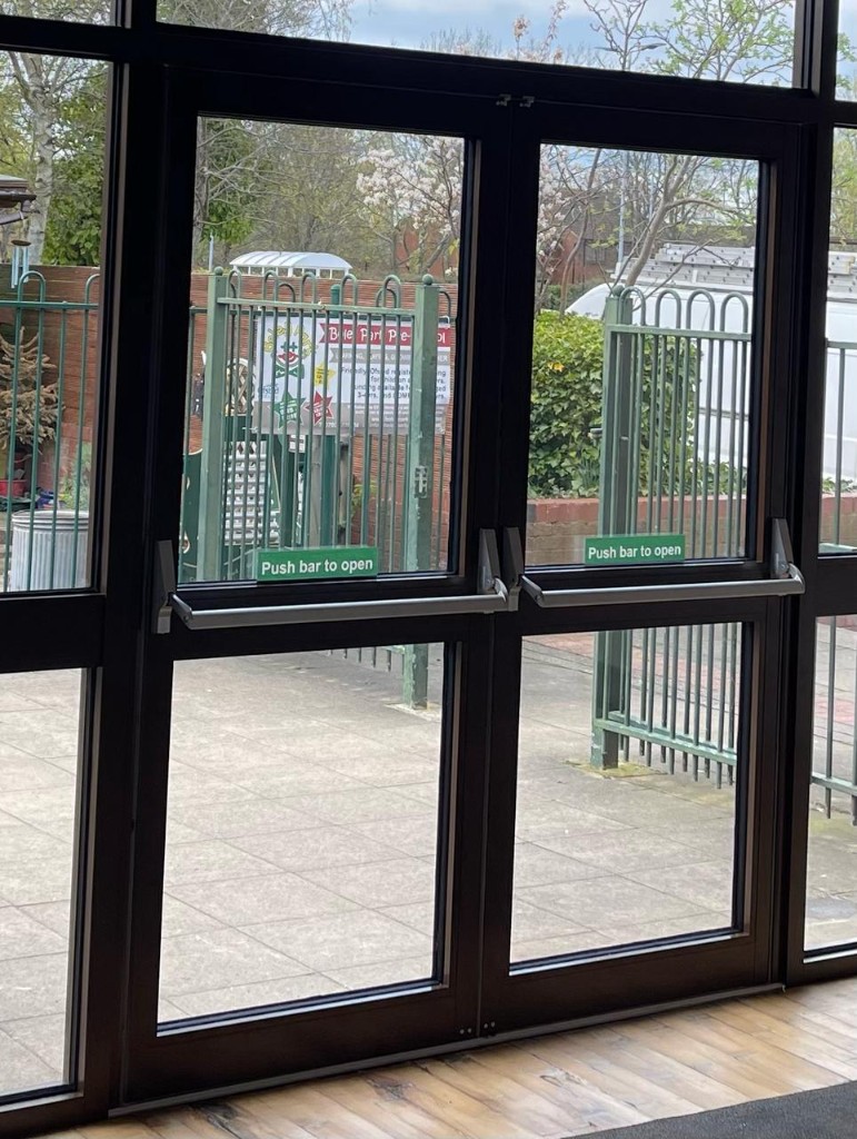 Black aluminium double fire exit doors with Axim panic bars and push bar to open signage at Boley Park Community Hall in Lichfield