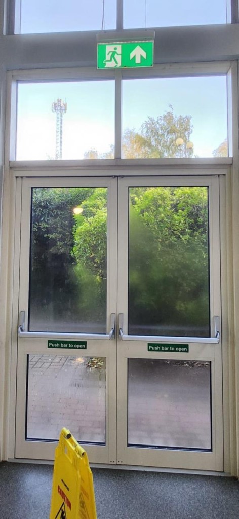 White aluminium double fire exit doors with Axim panic bars & push bar to open signage at DoubleTree by Hilton in Dartford, Kent