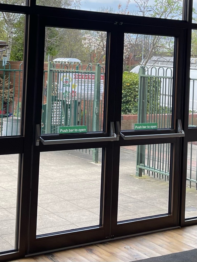 Dark aluminium double fire exit doors with panic bars and push bar to open signage viewed from a commercial building interior
