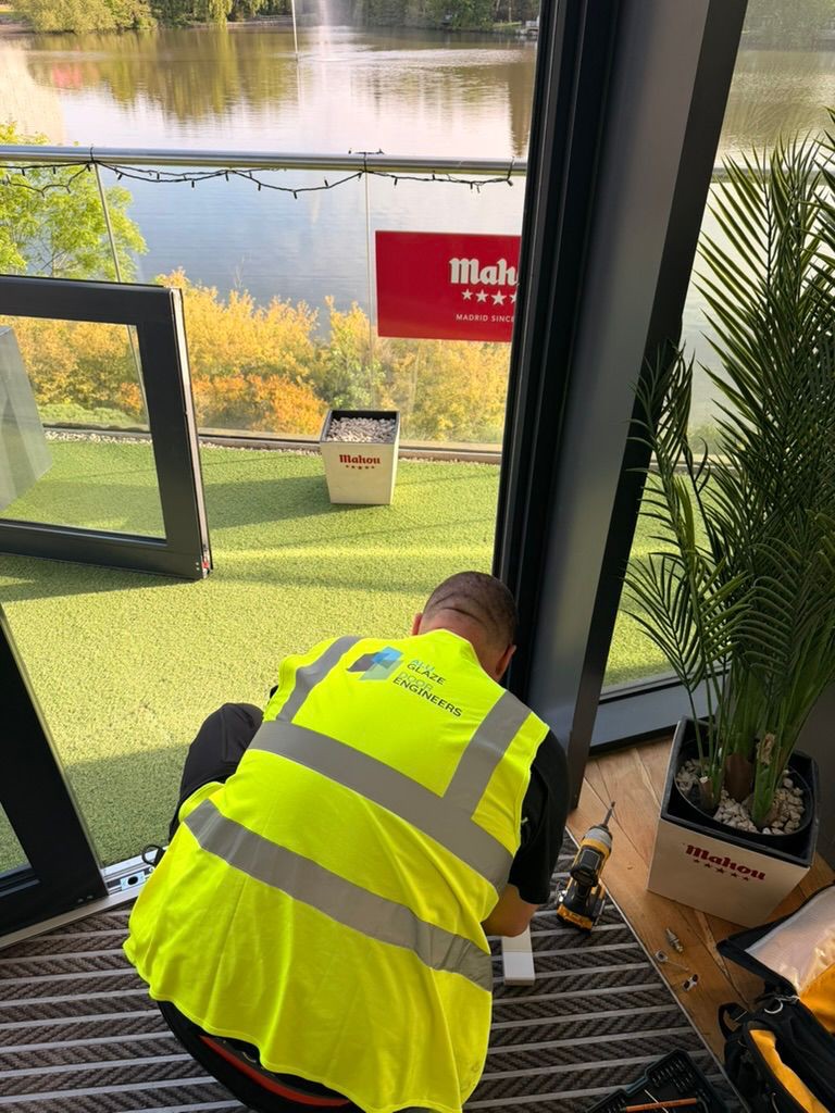 Door Engineers technician in high-visibility gear repairing commercial glass door hardware on site