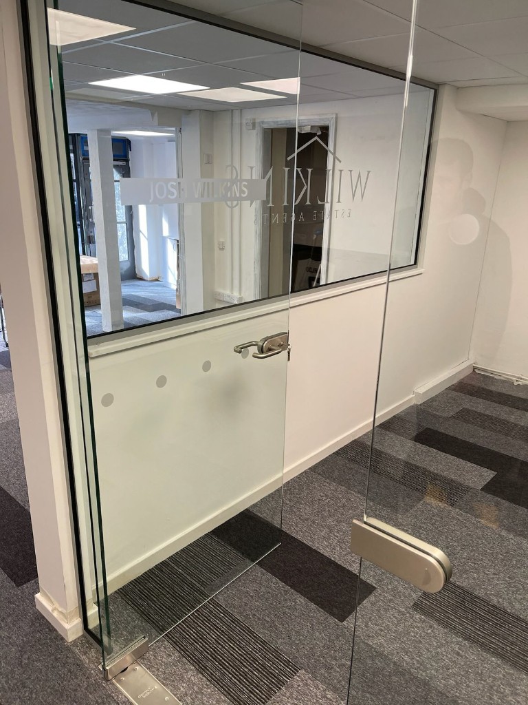 Frameless glass door with silver patch fittings, floor pivot & horizontal pull handle in a commercial office