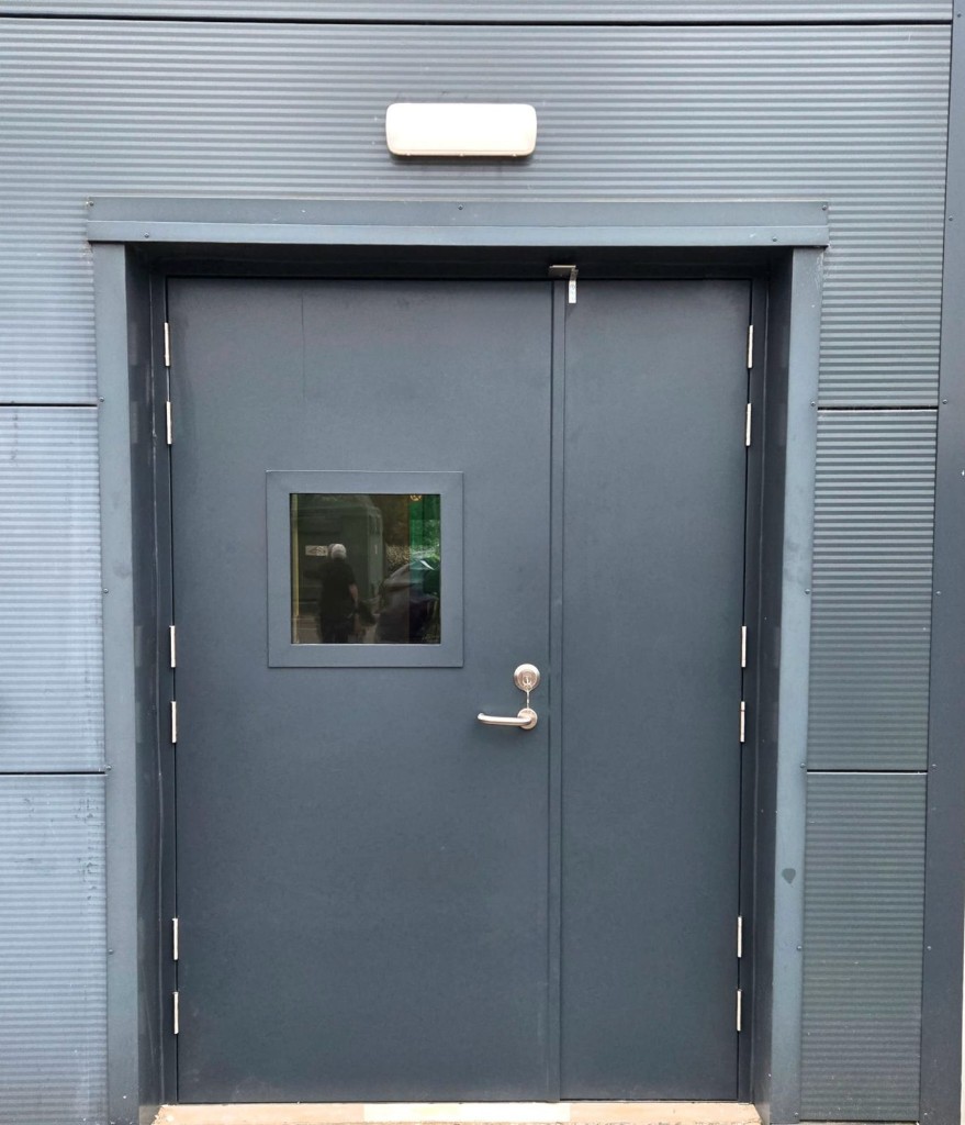 Grey steel double doors with lever handle, cylinder lock & vision panel on a commercial building