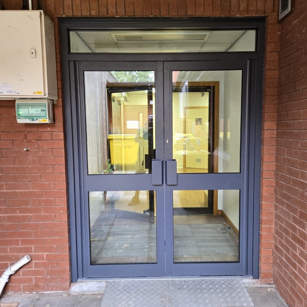 Anthracite powder-coated aluminium double entrance doors with glazed panels and pull handles set in a commercial brick building