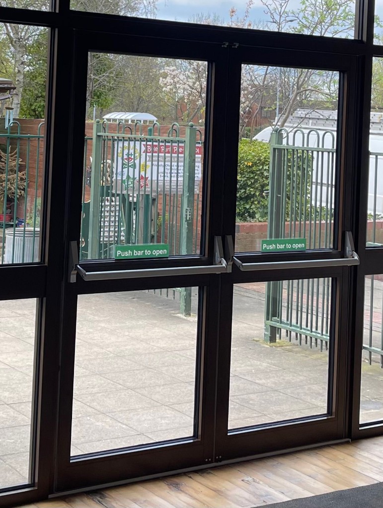 Double aluminium fire exit doors with panic bars & push-bar-to-open signage at a commercial building