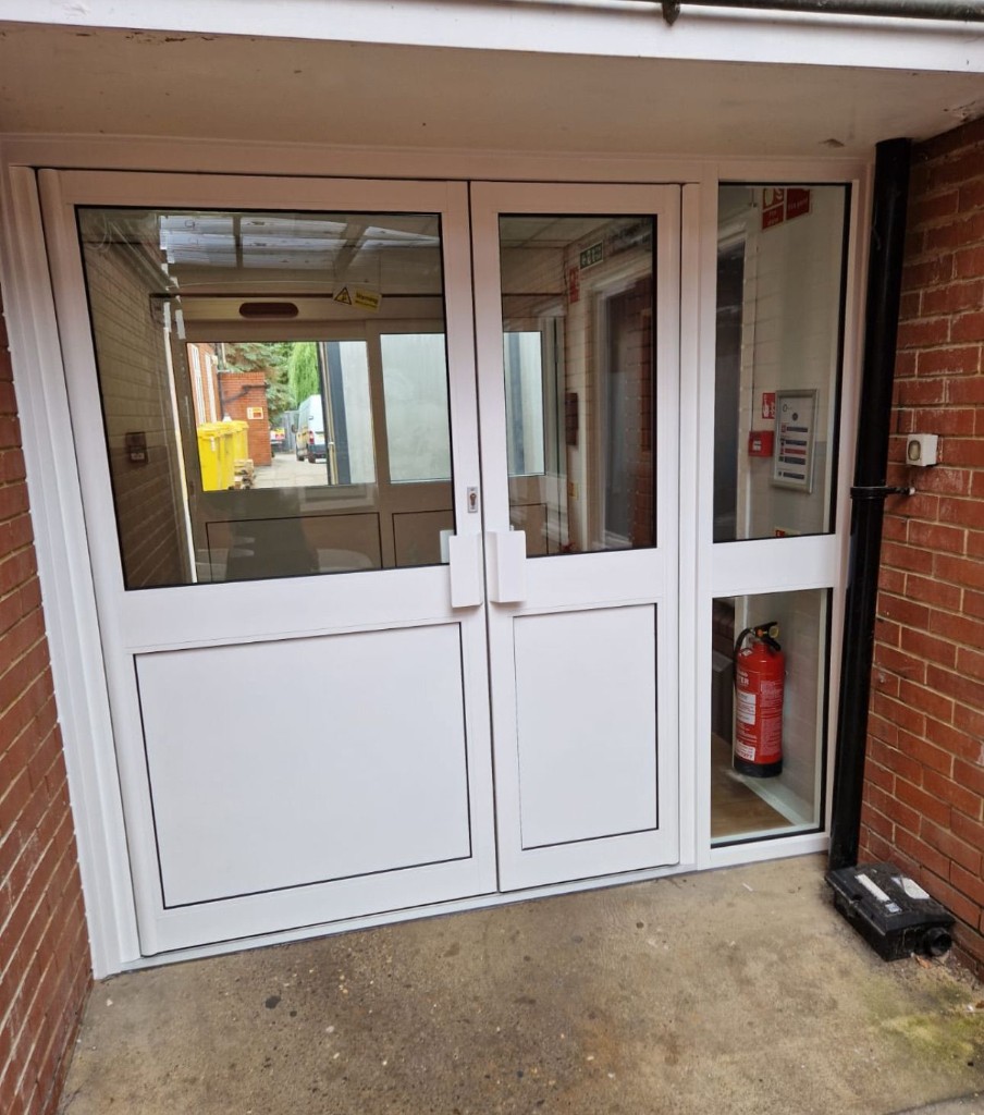 White aluminium double doors with glazed panels & sidelight set in a commercial brick entrance