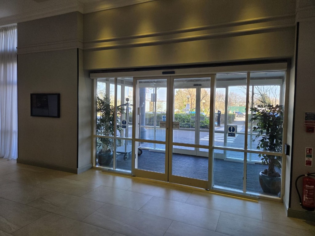 Automatic sliding glass doors with header operator, drive system & overhead activation sensor in a commercial entrance