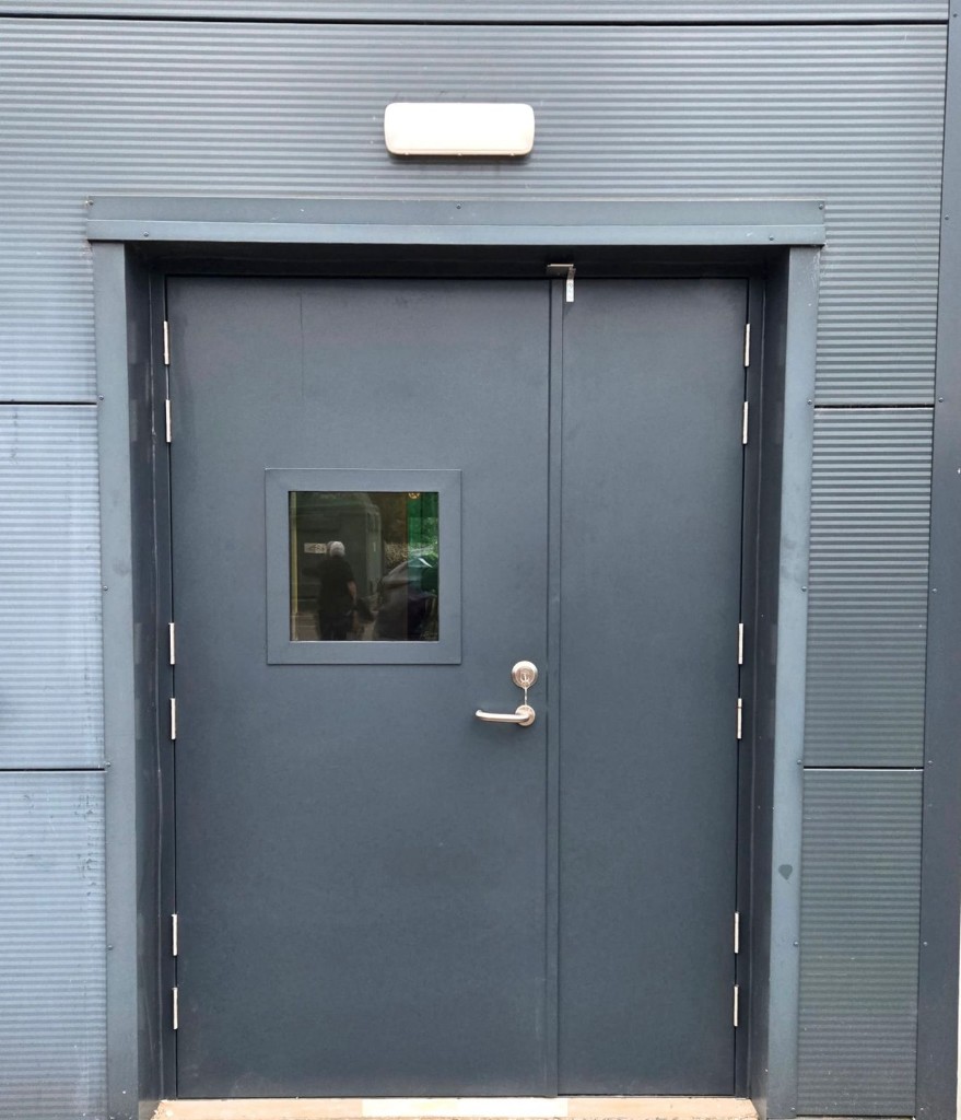 Charcoal powder-coated steel double security doors with lever handle, lock and vision panel on an industrial commercial building