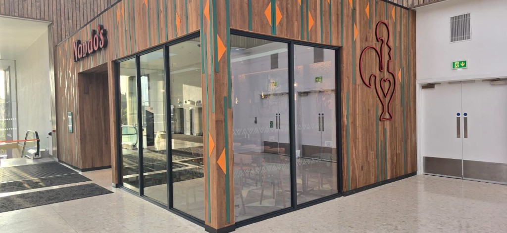 Nando's aluminium and glazed corner shopfront with dark framing and wood-clad fascia in a shopping centre