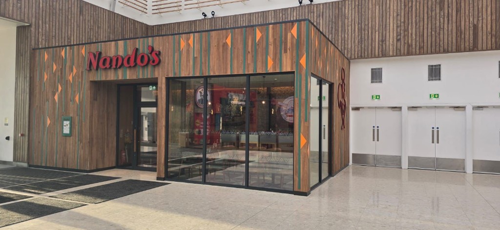 Nando's restaurant aluminium shopfront with black framed glazing, wood cladding & illuminated branding at Merry Hill shopping centre