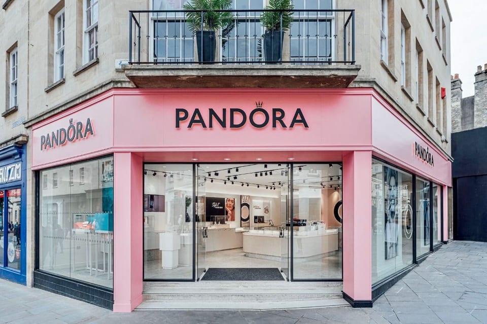 Pandora retail store aluminium shopfront with pink fascia, frameless glass entrance doors & powder-coated patch fittings on a Bath stone corner building