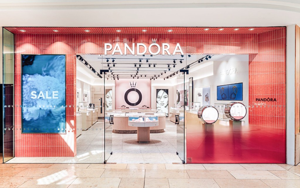 Pandora retail store shopfront with pink tiled cladding, glass entrance doors & illuminated branding at Bluewater Lower Mall