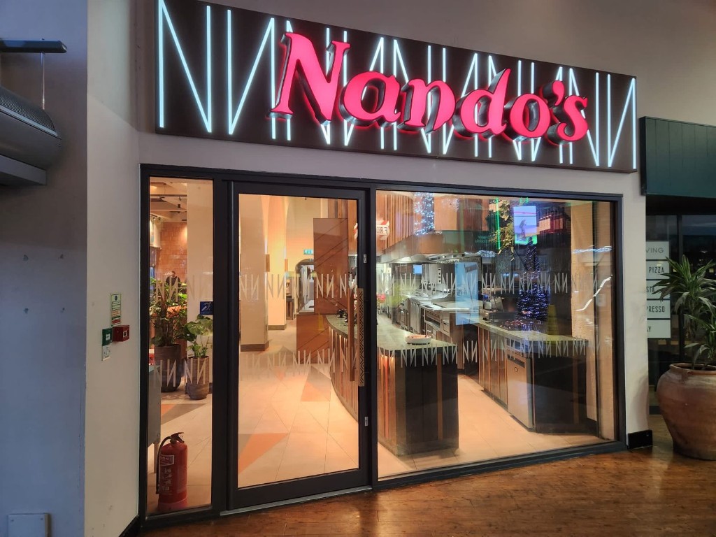 Nando's Aluminium Shopfront With Dark Framed Entrance Door, Glazed Panels And Illuminated Signage In A Shopping Centre